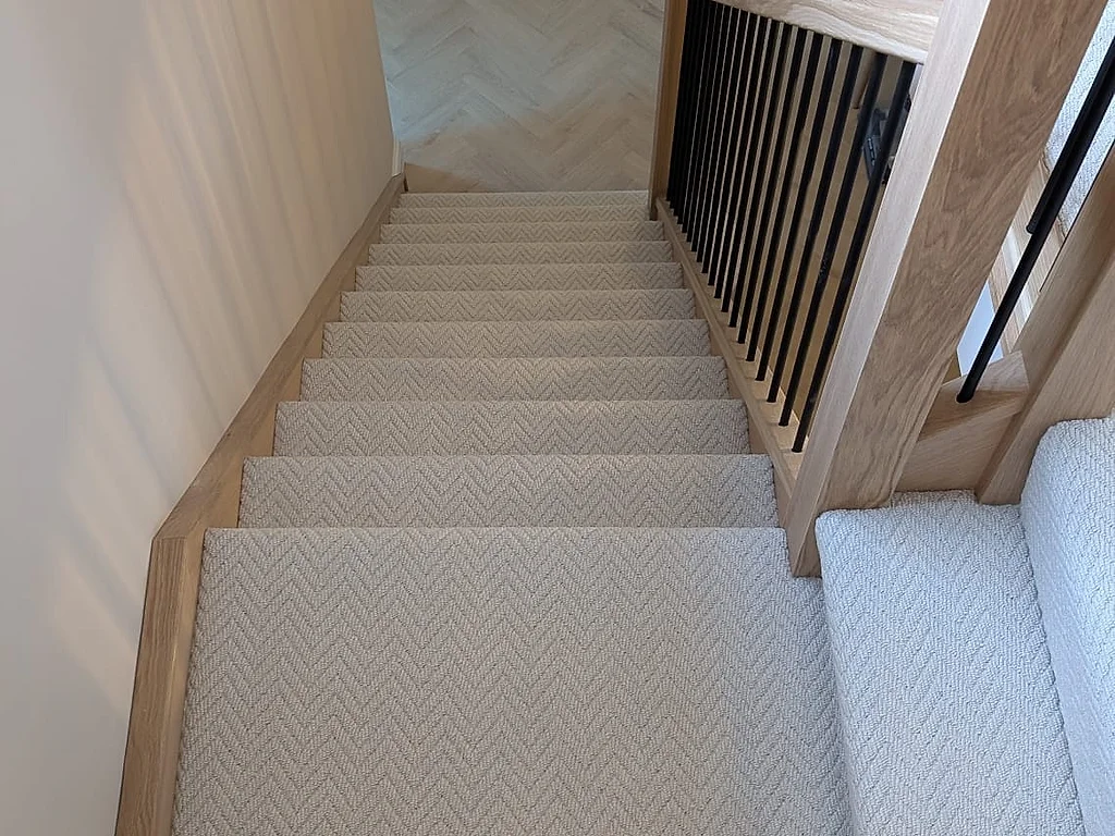 Cream herringbone carpet fitted on a staircase and landing with oak handrails