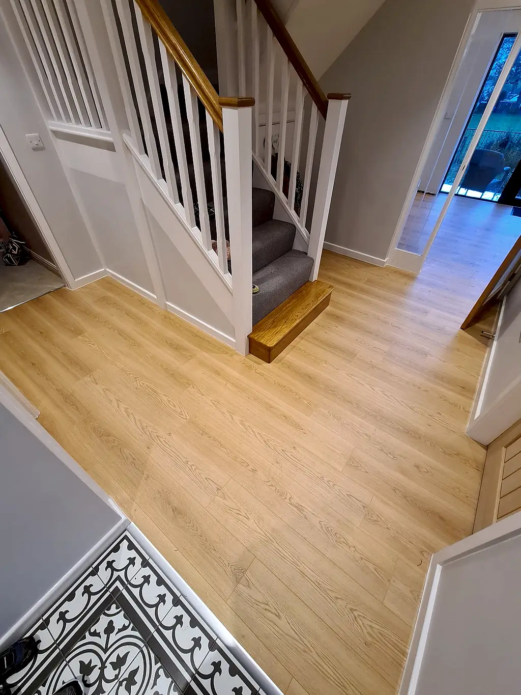 Oak effect laminate hallway floor with carpeted stairs and a patterned vinyl doorway