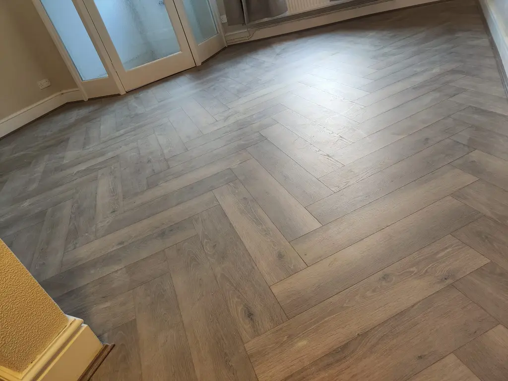 Grey oak herringbone flooring fitted across a room with glazed doors